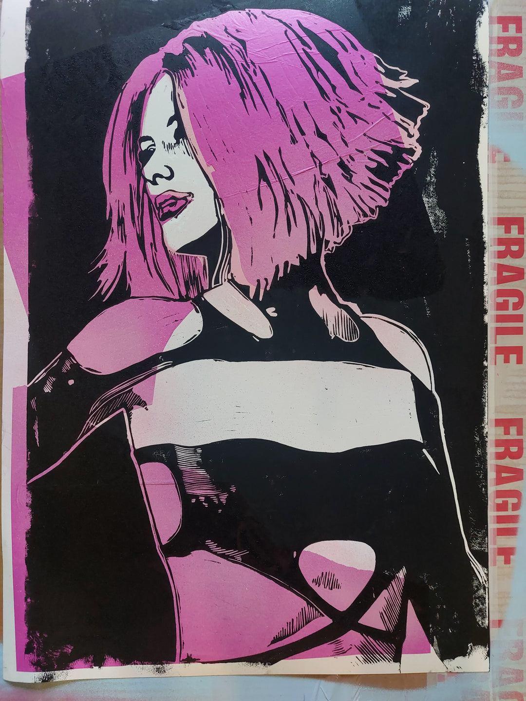 Linocut and spray paint portrait of a woman with voluminous pink hair, styled in a bold graphic bob. She wears a black cut-out latex top with high contrast light and shadow, set against a deep black backdrop. The piece is edged with raw textures and layered with printed “FRAGILE” tape along the right border—adding a punk-inspired, tactile element to the composition.