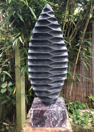 Bivalve Blade by Brendan Cullen, a tall hand-carved Kilkenny limestone sculpture with a tapered, leaf-like form and precise, rhythmic ridges reminiscent of shells or ancient fossils, mounted on a polished marble base.