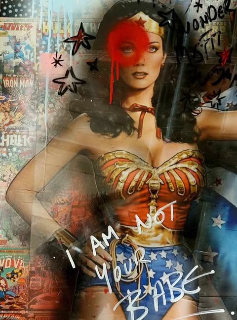 WONDER BABE — a bold one-off mixed media artwork featuring Wonder Woman against a collage of vintage comic book covers, overlaid with spray-painted stars, graffiti text, and a striking red mark across her eye. The phrase "I AM NOT YOUR BABE" is scrawled defiantly across the lower half.
