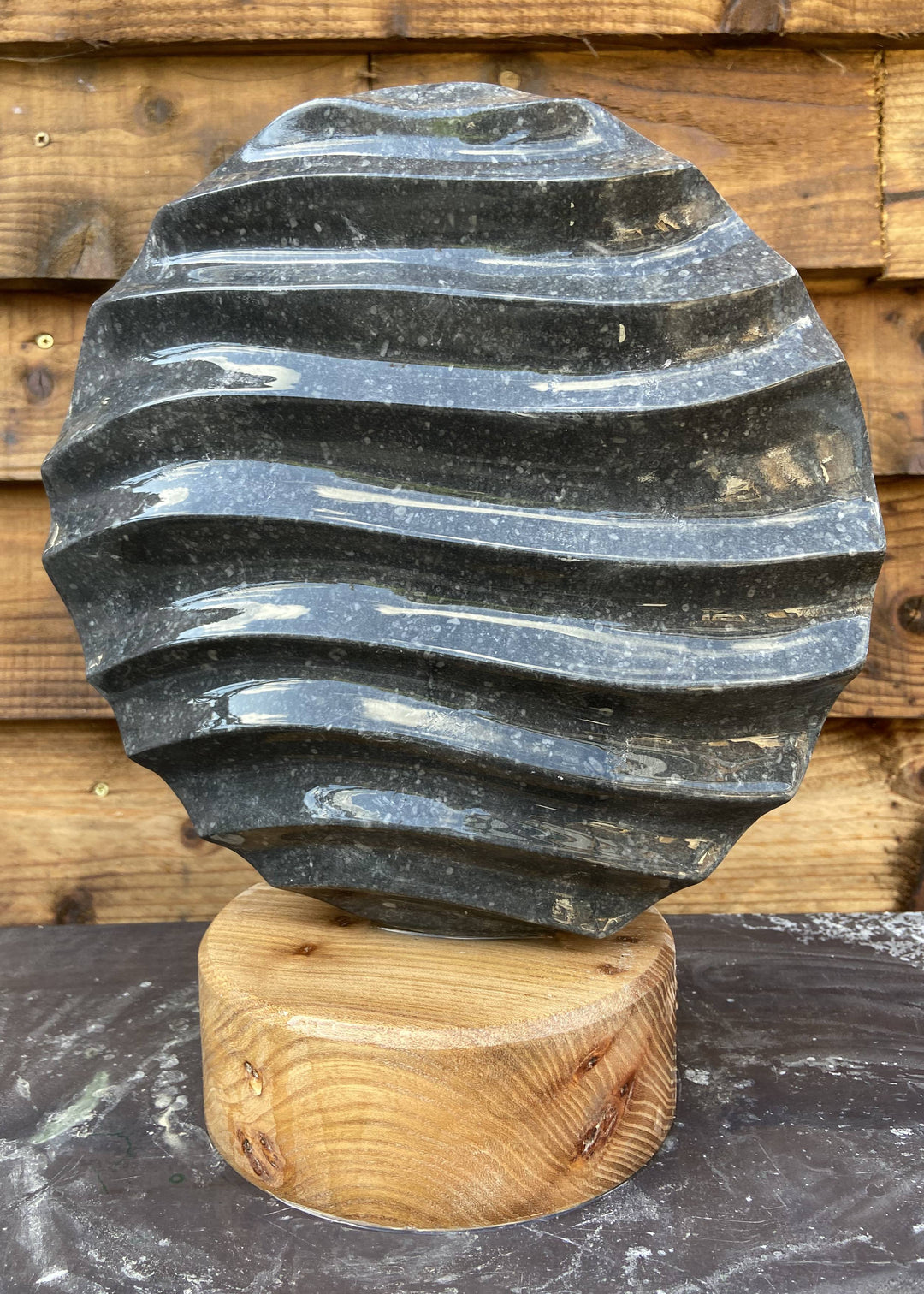 Flow 2 by Brendan Cullen, a compact hand-carved Kilkenny limestone sculpture with undulating wave-like ridges across its circular form, set on a smooth round wooden base.