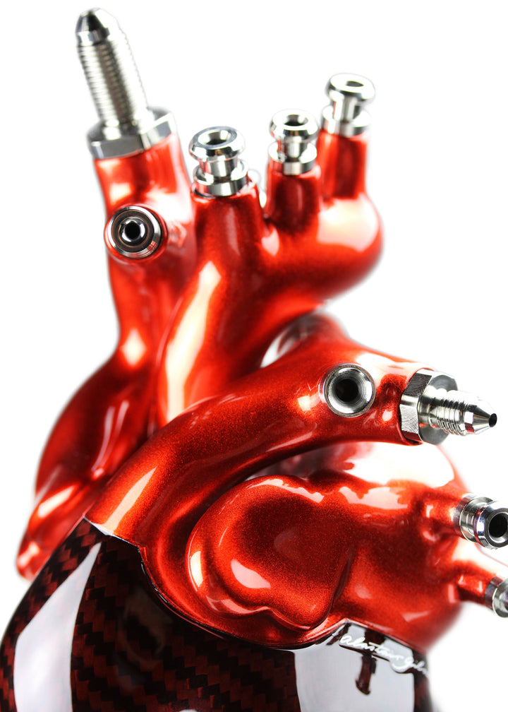 A vivid heart sculpture by Alastair Gibson, crafted from red-tinted 2x2 twill carbon fibre and finished with 3D-printed ABS atriums. Featuring titanium fuel and hydraulic fittings from Grand Prix cars, it fuses organic form with motorsport engineering. Finished in deep racing red with a UV-resistant gloss, it’s desk-mounted on a polished granite base with a stainless steel hydraulic support—blending precision with striking visual impact.