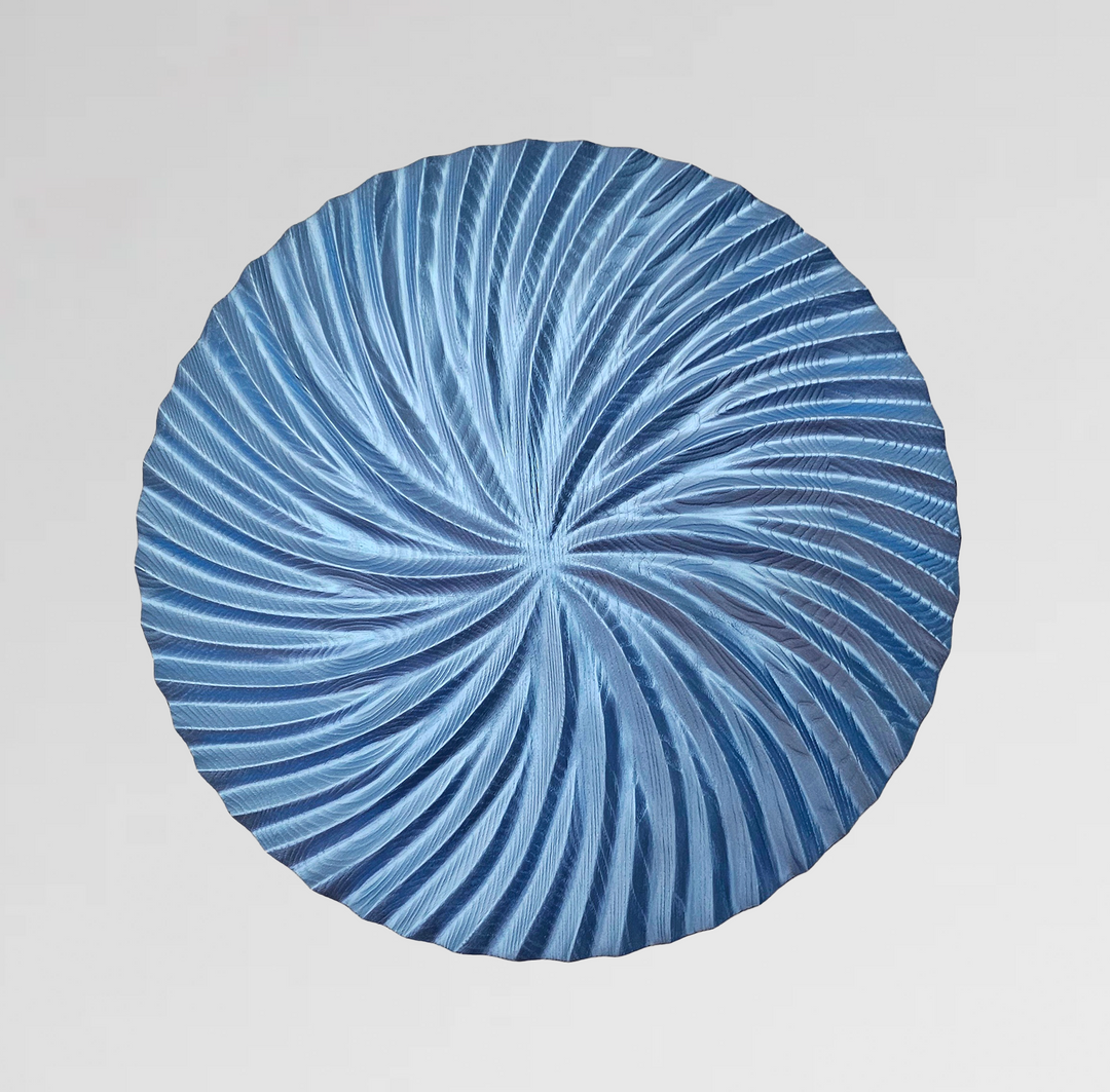 Round blue wall sculpture with intricate swirling carved patterns radiating from the centre.