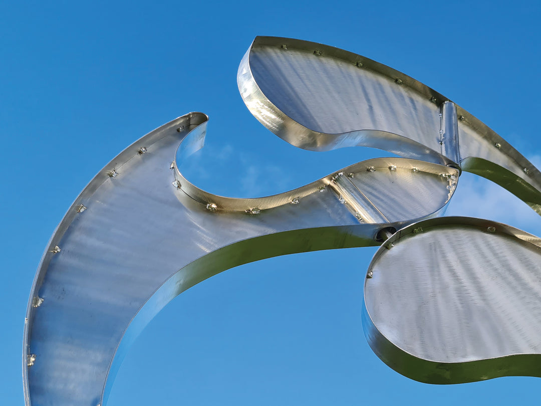 Abstract stainless steel kinetic sculpture with rotating, wind-driven elements and curved forms designed for outdoor movement