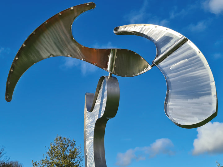 Abstract stainless steel kinetic sculpture with rotating, wind-driven elements and curved forms designed for outdoor movement