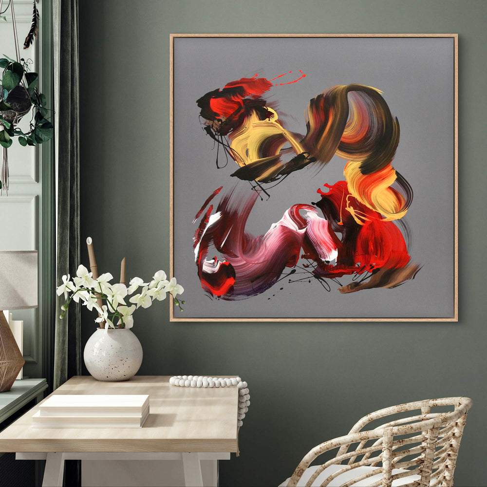 An expressive abstract acrylic painting on square canvas featuring bold, gestural brushstrokes in red, magenta, gold, burnt sienna, and black. The background is a smooth grey taupe, offering a neutral contrast to the vivid, swirling forms. The composition conveys dynamic movement and emotion, with layered, ribbon-like textures and flicks of paint that give a sense of energy and rhythm.