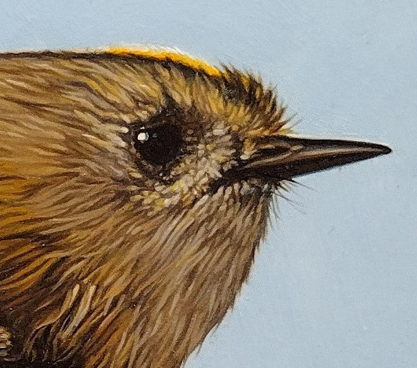 Hyperrealistic oil painting of a goldcrest perched on a blossom-covered branch, set against a soft blue background. The bird's golden crest and intricate feather detail are rendered with striking precision, accompanied by vivid red buds and lush green leaves.