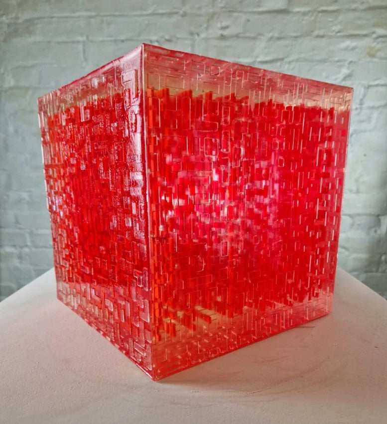 A one-off sculptural cube by Richard Slee, constructed from neon red acrylic and clear resin. The work features a dense, layered grid pattern that plays with light, depth, and shadow—creating a luminous, architectural object with a strong geometric presence. The cube glows from within, drawing the viewer into its intricate interior.