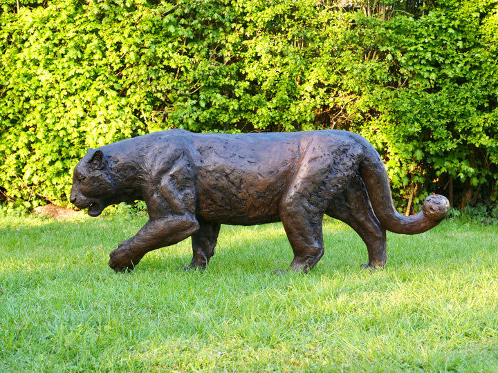 ‘Bloodline’ Amur leopard sculpture by Jamie Lord, life-size cold cast bronze of a leopard walking mid-stride with raised paw, textured dark bronze surface set outdoors on grass against green foliage