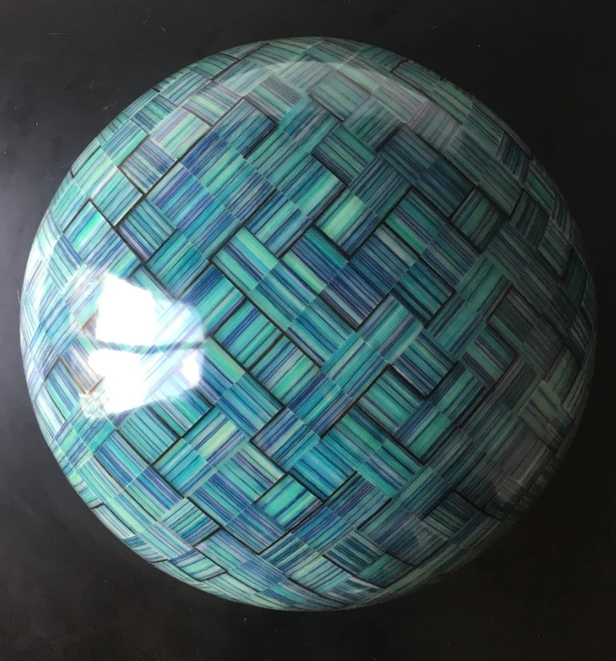Sculptural hemisphere titled “Orbtration in Blue” by Richard Slee, composed of interlocked cubes made from layered polypropylene sheets. The surface displays a striking woven pattern of cool-toned blues and greens, with a subtle glow from an internal light source. The piece shifts in presence under different lighting, revealing rich texture and depth.
