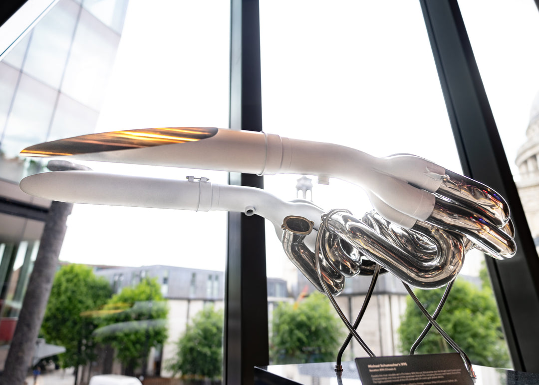 Highly polished sculptural artwork by Mike O’Connor crafted from the authentic race-used exhaust system of Michael Schumacher’s 1995 Benetton B195 Formula One car. The piece features flowing Inconel and stainless-steel pipes with mirror-finished chrome surfaces and 24-karat gold interior detailing, mounted on a sleek stand. A striking one-of-one collector’s piece 