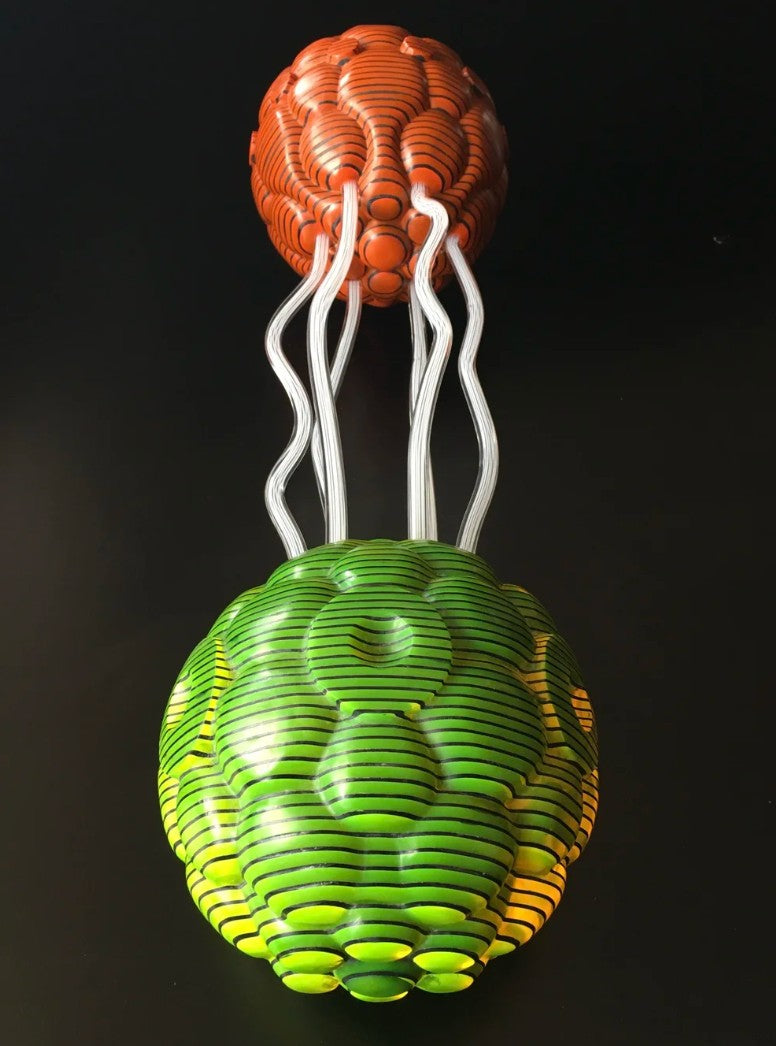 Abstract sculpture composed of two spherical forms—one in vivid orange, the other in bright green—connected by clear, wavy acrylic rods. Each orb is crafted from meticulously carved layers of acrylic sheets, forming a rippled, cellular surface. The vibrant colours and undulating lines create a dynamic visual interplay and sense of movement against a black backdrop.