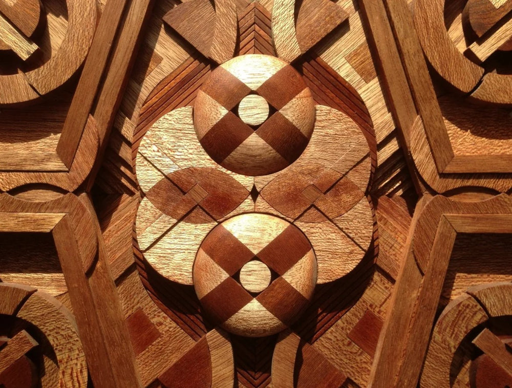 Intricately carved geometric wall sculpture by Richard Slee, made from Meranti wood in layered radial symmetry. The piece features intersecting circles, angles, and sculpted depth, with natural reddish-brown wood tones enhancing its three-dimensional, architectural feel.