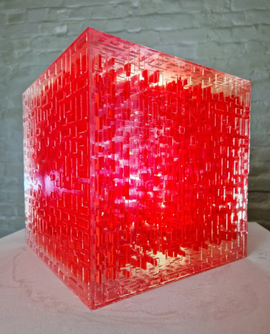 A one-off sculptural cube by Richard Slee, constructed from neon red acrylic and clear resin. The work features a dense, layered grid pattern that plays with light, depth, and shadow—creating a luminous, architectural object with a strong geometric presence. The cube glows from within, drawing the viewer into its intricate interior.