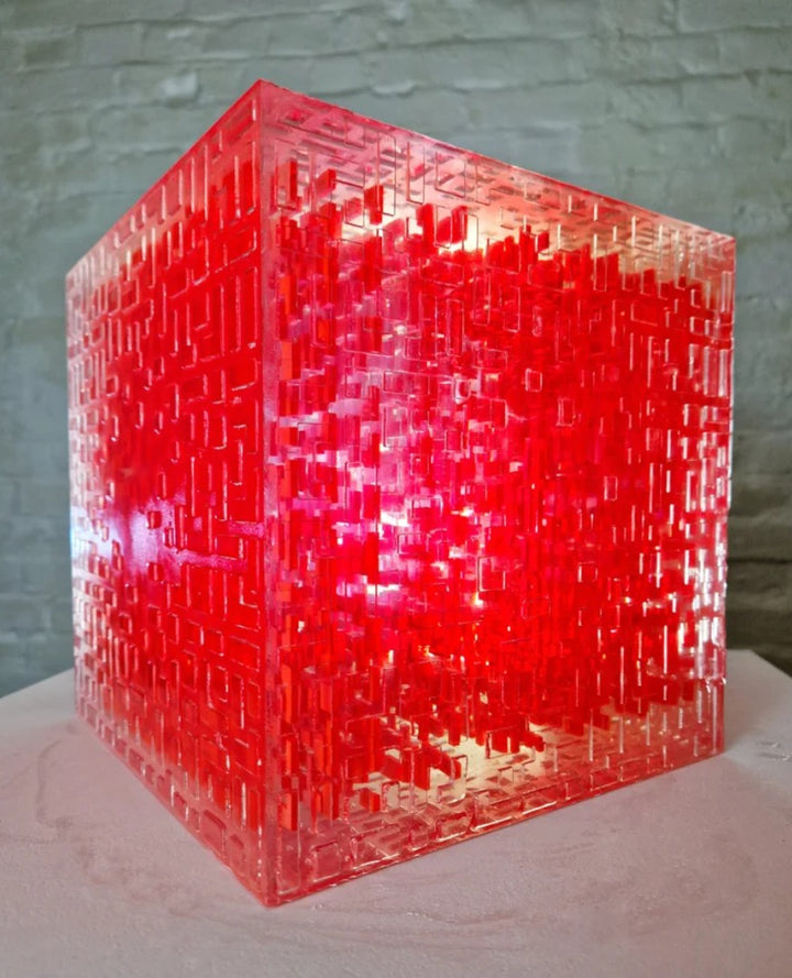 A one-off sculptural cube by Richard Slee, constructed from neon red acrylic and clear resin. The work features a dense, layered grid pattern that plays with light, depth, and shadow—creating a luminous, architectural object with a strong geometric presence. The cube glows from within, drawing the viewer into its intricate interior.
