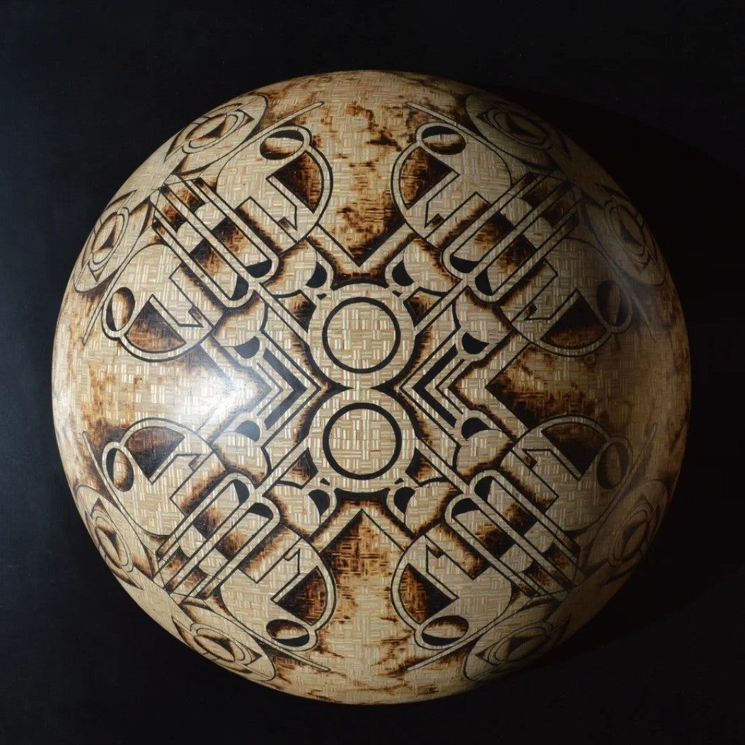 Intricately engraved hemispherical sculpture by Richard Slee titled “New Horizons Approaching.” Crafted from square 9mm plywood and shaded using a controlled burn technique, the surface features symmetrical, abstract motifs inlaid with black putty. The design has a radial, orbital quality with complex geometric lines and scorched textures, creating a striking contrast between natural wood tones and dark patterning.