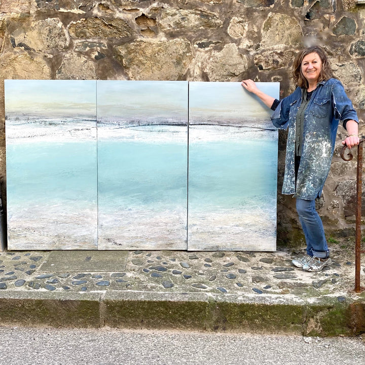 'Across The Bay, St Ives' by Heather McAlpine, an original large-scale triptych seascape painting in acrylic on canvas inspired by the panoramic beauty of St Ives Bay, Cornwall. Three connected panels depict pale turquoise waters, silvery shoreline and soft grey skies, capturing the shifting light, tide and tranquillity of the Cornish coast in an immersive contemporary composition.