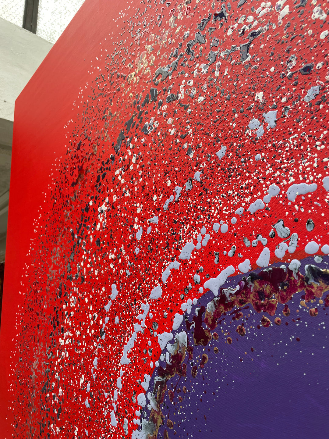 Large abstract painting “Ellipsis” by Swarez — bold square composition with a deep violet central circle surrounded by concentric rings of paint droplets and splashes on a vivid matte red background. Energetic, dynamic halo effect created by spin technique.