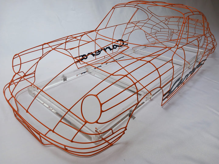 Handcrafted Porsche 911 2.7 RS wire sculpture by Chris Twitchell, finished in vivid Tangerine orange with black Carrera script. This detailed artwork captures the iconic pre-impact bumper 911 form — from its classic round headlights to the signature ducktail spoiler — reimagined as a precision-engineered wireframe sculpture that celebrates Porsche’s timeless design and performance heritage.