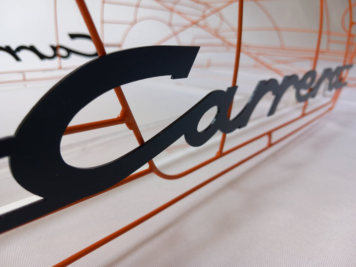 Handcrafted Porsche 911 2.7 RS wire sculpture by Chris Twitchell, finished in vivid Tangerine orange with black Carrera script. This detailed artwork captures the iconic pre-impact bumper 911 form — from its classic round headlights to the signature ducktail spoiler — reimagined as a precision-engineered wireframe sculpture that celebrates Porsche’s timeless design and performance heritage.