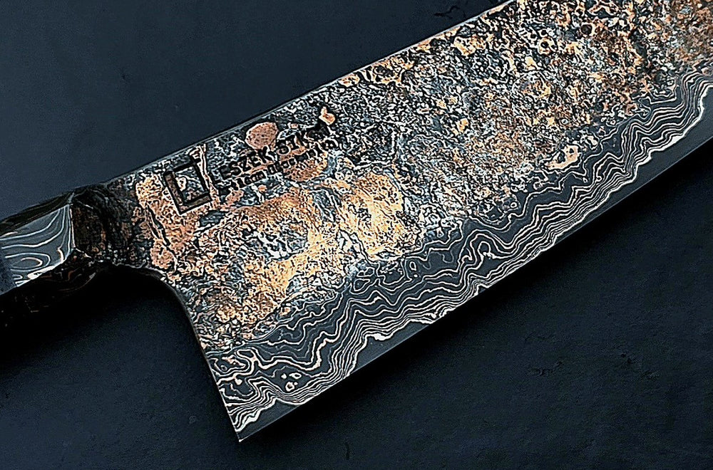 Close-up of a hand-forged Cu-Ni-Mascus Gyuto chef’s knife by Leszek Sikon, featuring an intricate 8120-layer Damascus pattern combining copper, nickel, brass, and high-carbon steels. The blade has a molten, marbled texture with visible copper sheen and an S-profile for food release, paired with a custom jeans micarta handle with embedded copper and steel mesh.