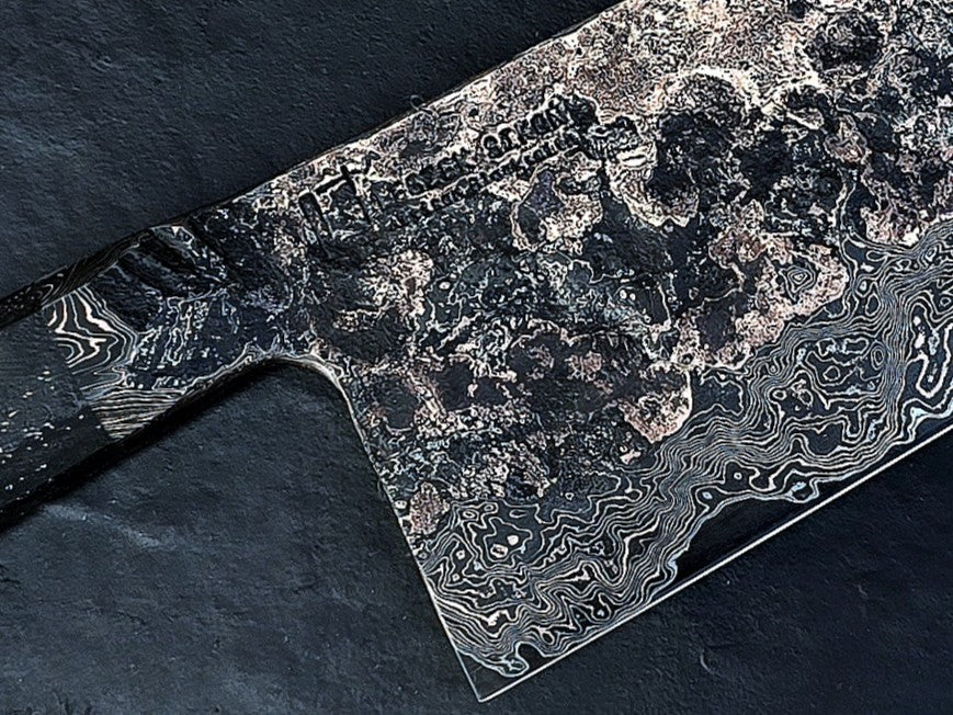 One-of-a-kind Cu-Ni-Mascus Nakiri knife by Leszek Sikon, showcasing 8120 layers of Damascus forged from Spicy White steel, O1 tool steel, copper, nickel, and brass. The blade features a rich, geological pattern with molten textures and wave-like lines, hand-forged over 100 hours with an S-profile for food release and finished with a custom jeans micarta handle embedded with copper and steel mesh.