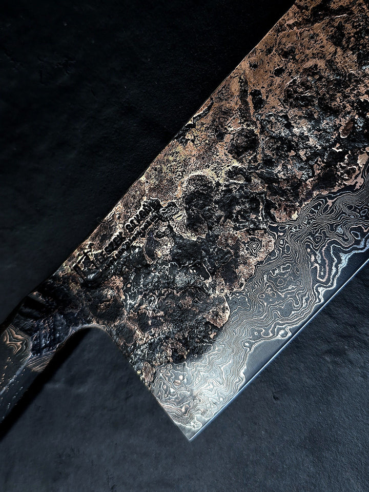 One-of-a-kind Cu-Ni-Mascus Nakiri knife by Leszek Sikon, showcasing 8120 layers of Damascus forged from Spicy White steel, O1 tool steel, copper, nickel, and brass. The blade features a rich, geological pattern with molten textures and wave-like lines, hand-forged over 100 hours with an S-profile for food release and finished with a custom jeans micarta handle embedded with copper and steel mesh.