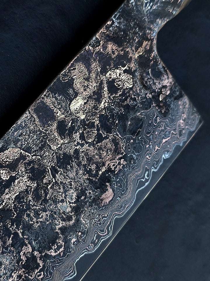 One-of-a-kind Cu-Ni-Mascus Nakiri knife by Leszek Sikon, showcasing 8120 layers of Damascus forged from Spicy White steel, O1 tool steel, copper, nickel, and brass. The blade features a rich, geological pattern with molten textures and wave-like lines, hand-forged over 100 hours with an S-profile for food release and finished with a custom jeans micarta handle embedded with copper and steel mesh.