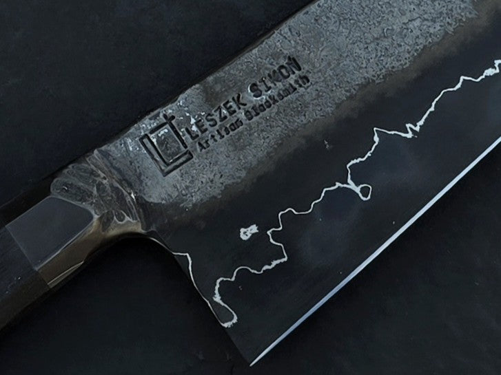 Leszek Sikon San Mai Chef Graphite Gyuto hand-forged chef’s knife featuring a dark San Mai carbon steel blade with visible hamon line and bog oak handle.