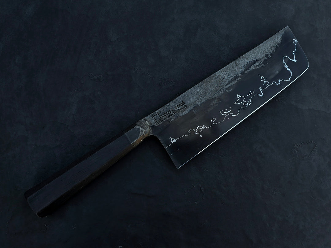 Leszek Sikon San Mai Graphite Nakiri hand-forged kitchen knife featuring a dark laminated carbon steel blade with visible hamon line and bog oak handle.