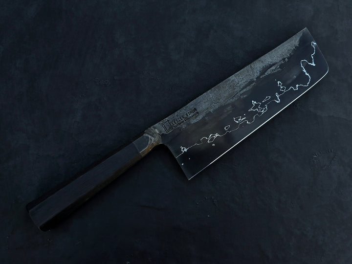 Leszek Sikon San Mai Graphite Nakiri hand-forged kitchen knife featuring a dark laminated carbon steel blade with visible hamon line and bog oak handle.