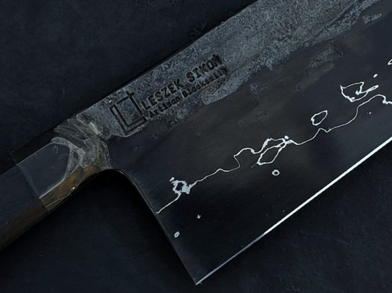 Leszek Sikon San Mai Graphite Nakiri hand-forged kitchen knife featuring a dark laminated carbon steel blade with visible hamon line and bog oak handle.
