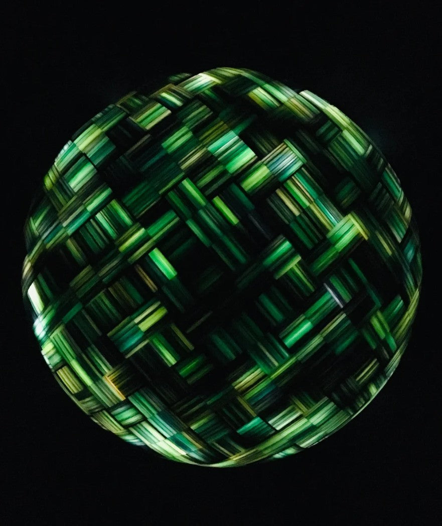 Sculptural hemisphere titled “Orbtration in Blue” by Richard Slee, composed of interlocked cubes made from layered polypropylene sheets. The surface displays a striking woven pattern of cool-toned blues and greens, with a subtle glow from an internal light source. The piece shifts in presence under different lighting, revealing rich texture and depth.