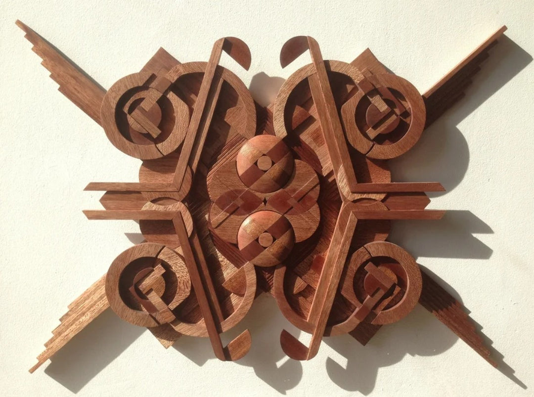Intricately carved geometric wall sculpture by Richard Slee, made from Meranti wood in layered radial symmetry. The piece features intersecting circles, angles, and sculpted depth, with natural reddish-brown wood tones enhancing its three-dimensional, architectural feel.