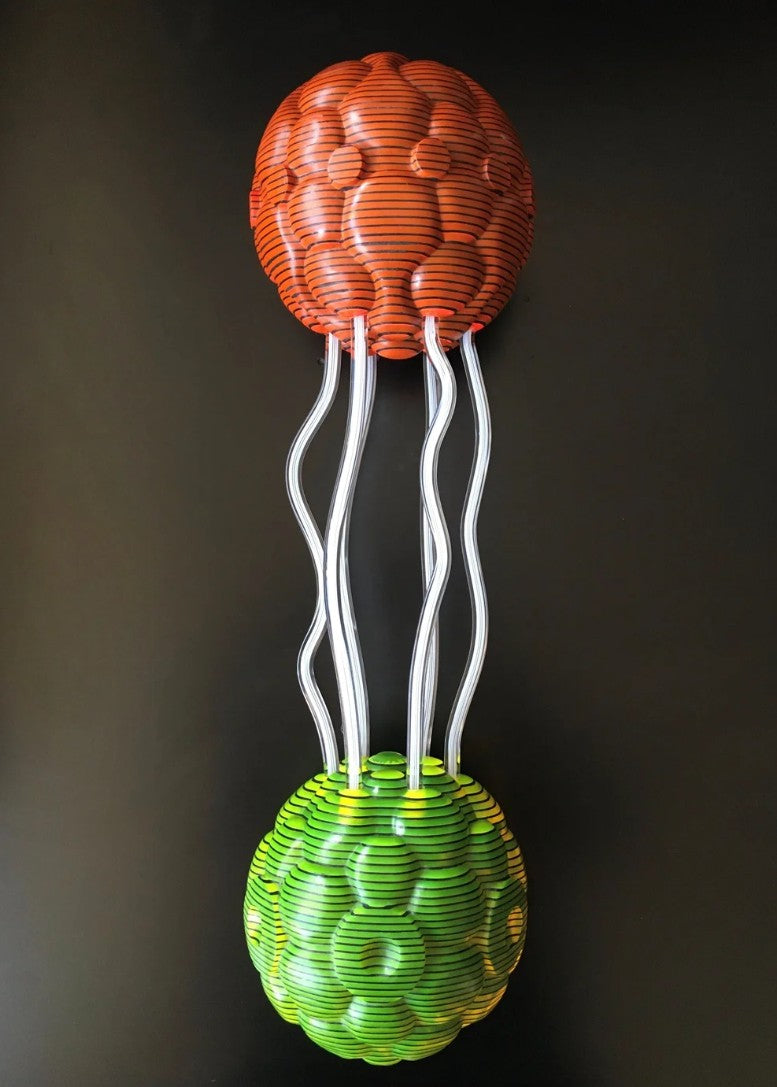 Abstract sculpture composed of two spherical forms—one in vivid orange, the other in bright green—connected by clear, wavy acrylic rods. Each orb is crafted from meticulously carved layers of acrylic sheets, forming a rippled, cellular surface. The vibrant colours and undulating lines create a dynamic visual interplay and sense of movement against a black backdrop.