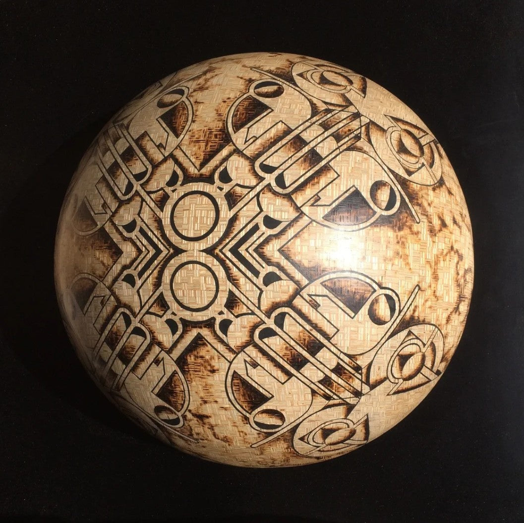 Intricately engraved hemispherical sculpture by Richard Slee titled “New Horizons Approaching.” Crafted from square 9mm plywood and shaded using a controlled burn technique, the surface features symmetrical, abstract motifs inlaid with black putty. The design has a radial, orbital quality with complex geometric lines and scorched textures, creating a striking contrast between natural wood tones and dark patterning.