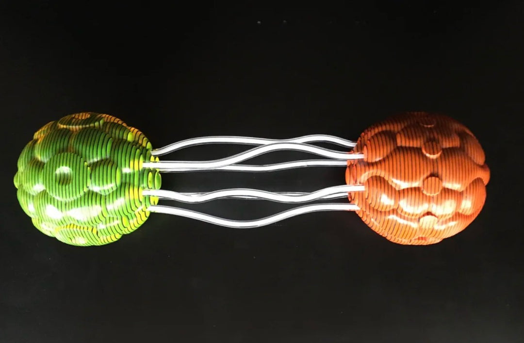 Abstract sculpture composed of two spherical forms—one in vivid orange, the other in bright green—connected by clear, wavy acrylic rods. Each orb is crafted from meticulously carved layers of acrylic sheets, forming a rippled, cellular surface. The vibrant colours and undulating lines create a dynamic visual interplay and sense of movement against a black backdrop.