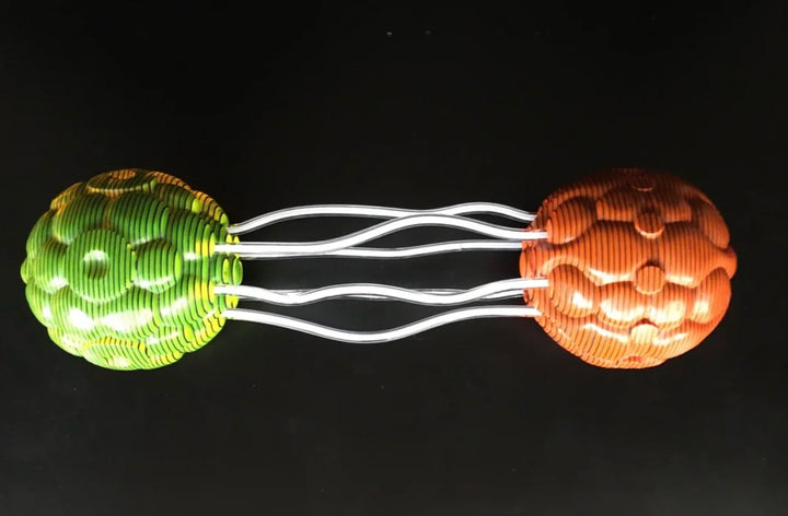 Abstract sculpture composed of two spherical forms—one in vivid orange, the other in bright green—connected by clear, wavy acrylic rods. Each orb is crafted from meticulously carved layers of acrylic sheets, forming a rippled, cellular surface. The vibrant colours and undulating lines create a dynamic visual interplay and sense of movement against a black backdrop.