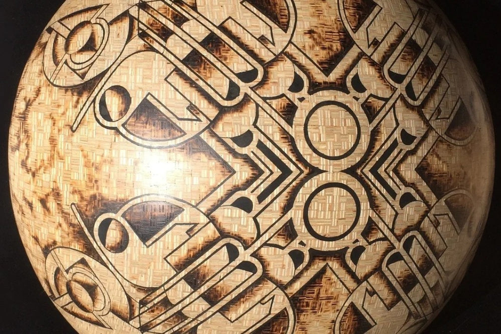 Intricately engraved hemispherical sculpture by Richard Slee titled “New Horizons Approaching.” Crafted from square 9mm plywood and shaded using a controlled burn technique, the surface features symmetrical, abstract motifs inlaid with black putty. The design has a radial, orbital quality with complex geometric lines and scorched textures, creating a striking contrast between natural wood tones and dark patterning.