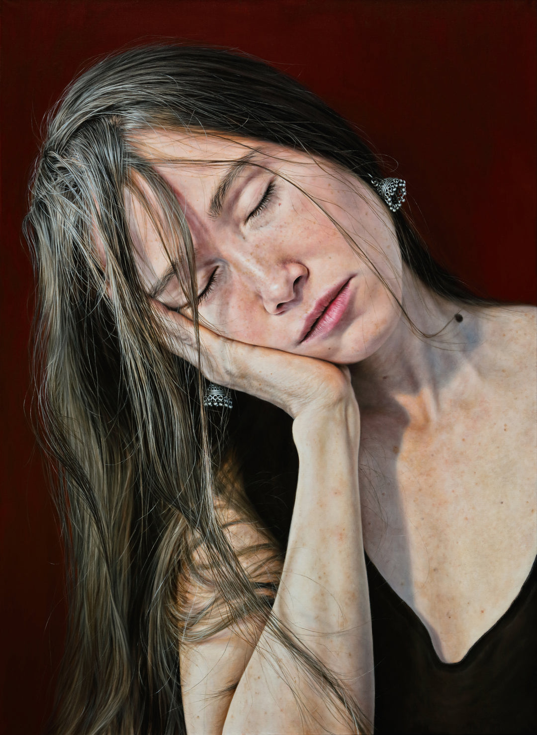 Arina Gordienko hyperrealist oil painting I Had a Dream, portraying a young woman with closed eyes and long brown hair falling across her face, resting her head in her hand, wearing a black top and silver earrings, against a deep red background. The work captures fragility, exhaustion, and dreamlike escape with extraordinary lifelike detail.