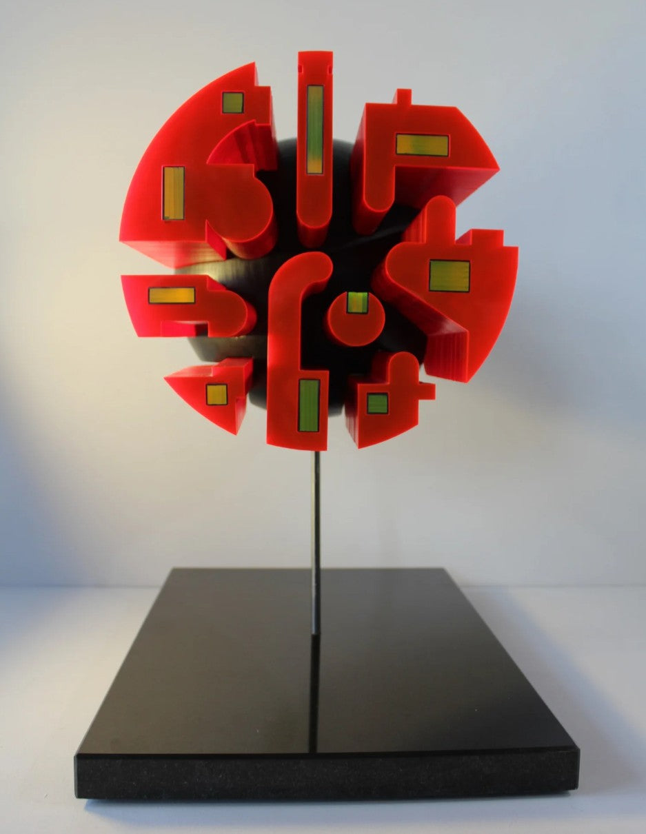 Futuristic sculptural form mounted on a black granite base, featuring a central spherical structure composed of layered neon red acrylic and matte black HIPS segments. The sculpture is precision-carved with bold geometric cut-outs and embedded reflective elements in green and yellow. Its striking contrast and luminous red glow give it the presence of an otherworldly artefact or machine, exuding personality and presence.