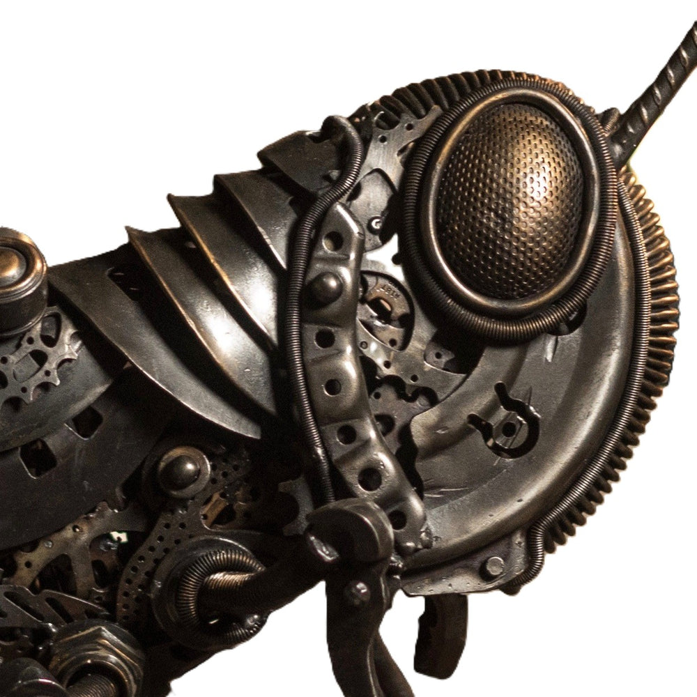 Mechanical grasshopper sculpture crafted from reclaimed metal and gears, displayed on a rustic workbench.