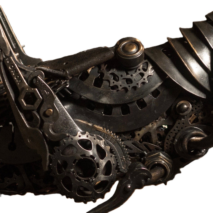 Mechanical grasshopper sculpture crafted from reclaimed metal and gears, displayed on a rustic workbench.