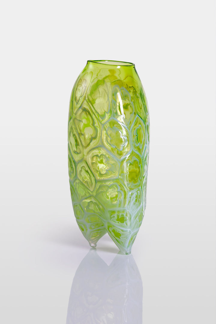 Tall handblown green glass sculpture with embossed floral motifs and a softly asymmetrical, pod-like form, resting on a reflective surface.