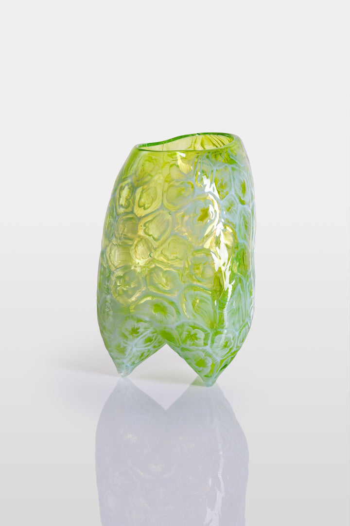 Handcrafted green glass vessel with organic floral embossing and a softly asymmetrical form, set against a white background with reflective base.