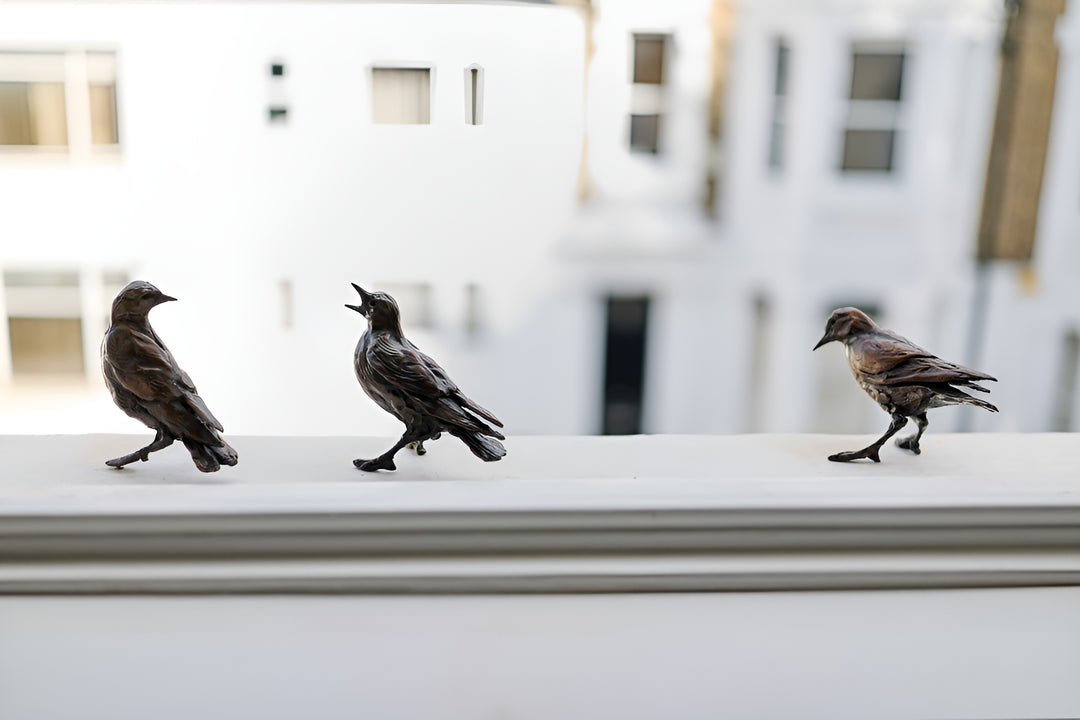 Jane Shaw Community Spirit bronze sculpture depicting a group of starlings perched along a ledge, each bird individually posed to suggest interaction, movement and communication. The figures vary subtly in stance - some alert, some mid-song - capturing the character and rhythm of urban bird life, with a naturalistic bronze finish that highlights feather texture and form against an architectural setting.