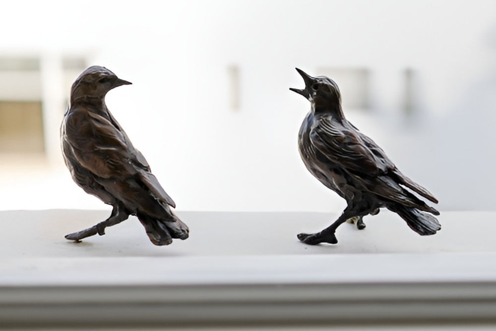 Jane Shaw Community Spirit bronze sculpture depicting a group of starlings perched along a ledge, each bird individually posed to suggest interaction, movement and communication. The figures vary subtly in stance - some alert, some mid-song - capturing the character and rhythm of urban bird life, with a naturalistic bronze finish that highlights feather texture and form against an architectural setting.