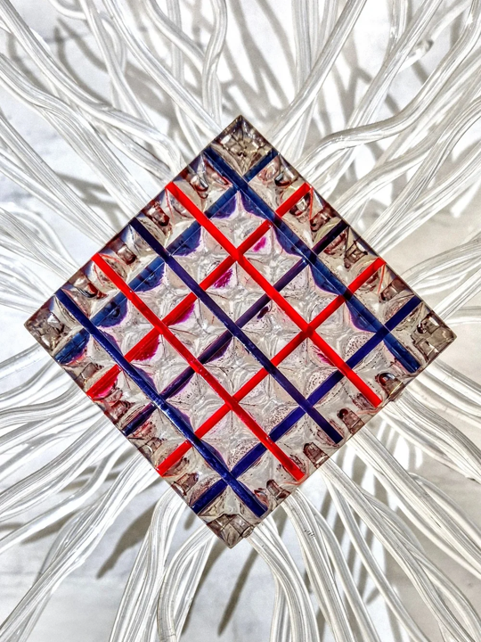 Large-scale sculptural artwork featuring a central geometric cube formed from layered resin in transparent red, blue, and clear tones. Radiating outward are dozens of transparent, sinuous tentacle-like extensions made of acrylic or resin tubing, tipped in black. The structure resembles an imagined extraterrestrial lifeform, with a visually striking symmetry and futuristic energy. Set against a white brick wall, the piece evokes themes of outer space, abstract biology, and the unknown.