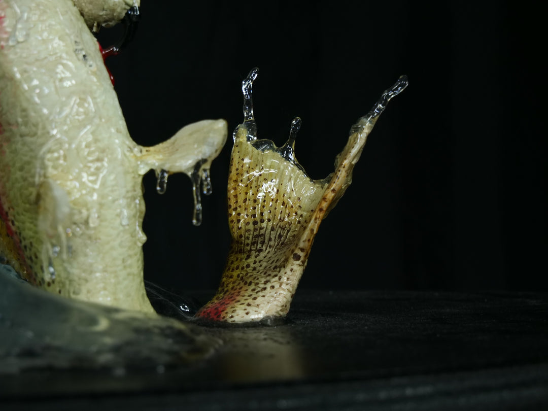 A dramatic paper sculpture of an osprey mid-flight, wings fully extended, clutching a rainbow trout in its talons. Featuring hand-cut, painted feathers in rich browns, creams, and ochres, with a vivid yellow eye and bold red markings on the fish. Set on a sculpted base representing water, with a fine outline of Scotland etched into the resin.