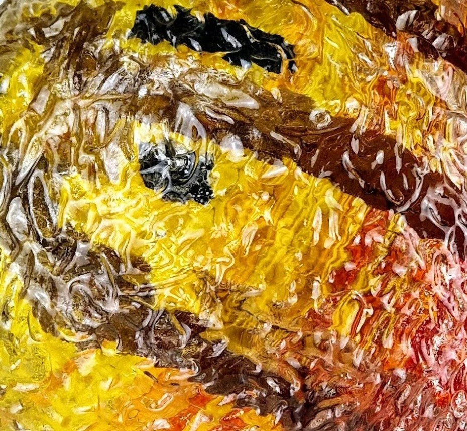 Spherical mixed media sculpture with a diameter of 32cm, composed of layered resin and ply wood. The outer surface features a textured, translucent finish with intricate swirling forms and embedded patterns. Vivid tones of amber, yellow, burnt orange, black and deep red create a celestial, planetary effect—suggesting a glowing sun or molten planet. The polished surface reflects light, adding depth and vibrancy to the overall form.
