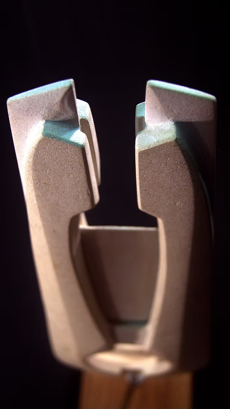 Stone sculpture featuring two tall, curved spires carved from Purbeck Thornback stone, set on a polished black granite base, connected by a narrow central opening with stainless steel elements, displayed against a dark background.